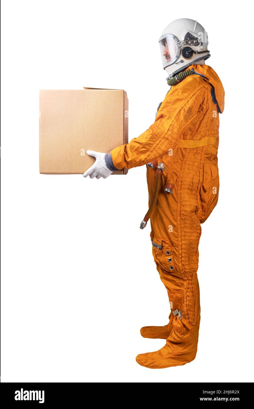 Astronaut wearing orange space suit and space helmet holding in hand brown cardboard box isolated on a white background. Delivery concept. Stock Photo