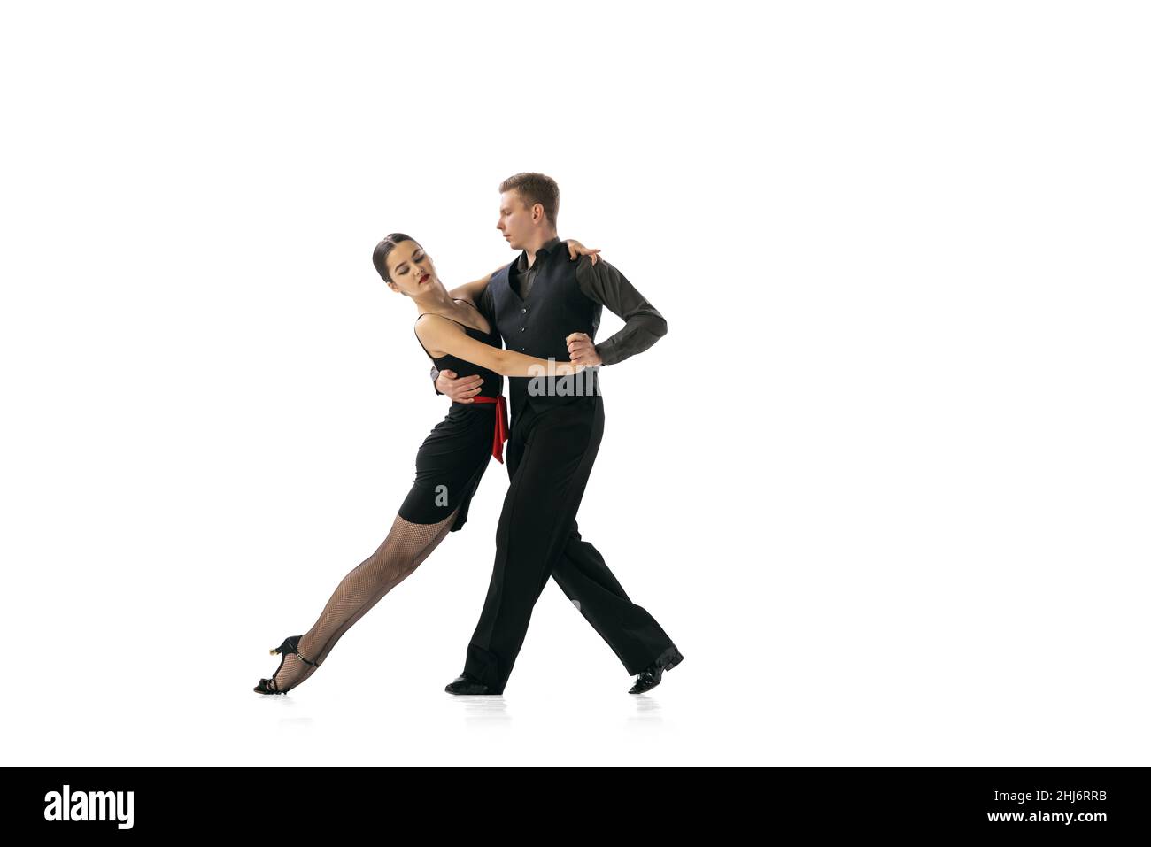 Beautiful sportive young man and woman dancing Argentine tango isolated on white studio background. Artists in black stage costumes Stock Photo