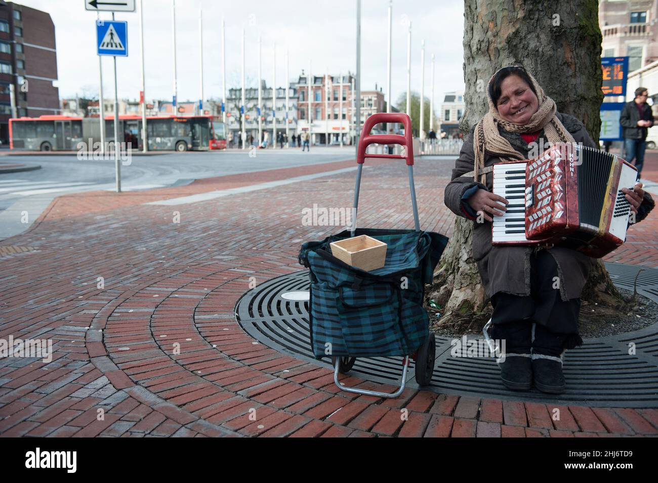 Haarlem, Netherlands. Roma woman playing her accordion at a railway station square to earn a buck or two a day. Roma men and women are en masse transported to Western European Countries to earn tips and scraps of money in various ways to support their lives in poverty and the Huma Trafficking Groups that bring them to the West. Stock Photo