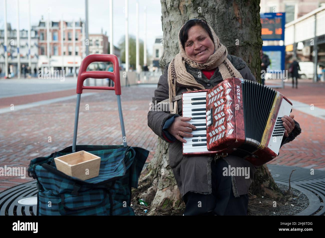 Haarlem, Netherlands. Roma woman playing her accordion at a railway station square to earn a buck or two a day. Roma men and women are en masse transported to Western European Countries to earn tips and scraps of money in various ways to support their lives in poverty and the Huma Trafficking Groups that bring them to the West. Stock Photo