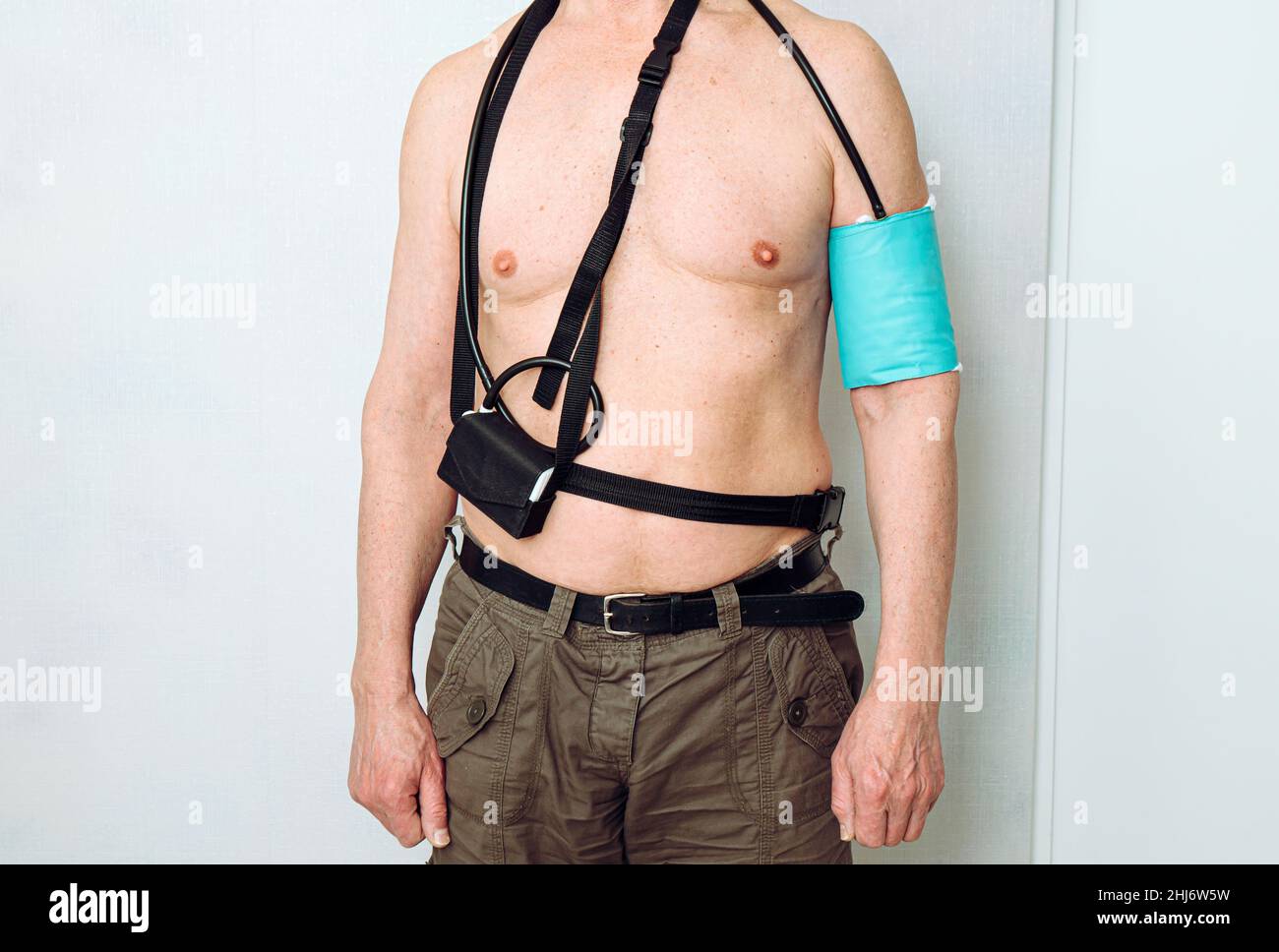 Body of a middle aged man using portable Ambulatory Blood Pressure Monitor (ABPM) for taking measurements during normal daily activities at home. Stock Photo