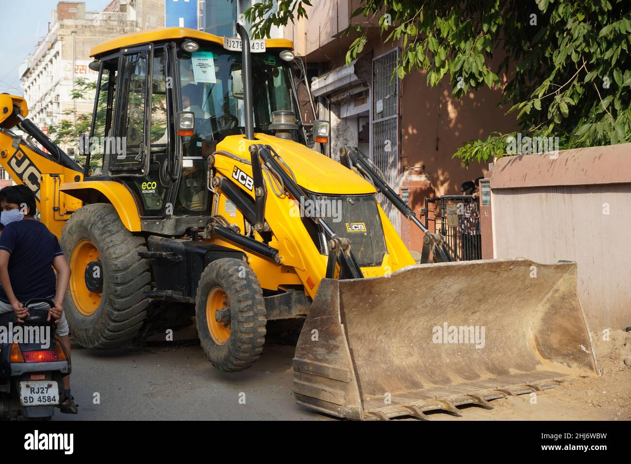 JCB earth moving machine working on a road. JCB bucket loader is repairing a section of a dirt road. Road is expanding in residential quarter. Theme o Stock Photo