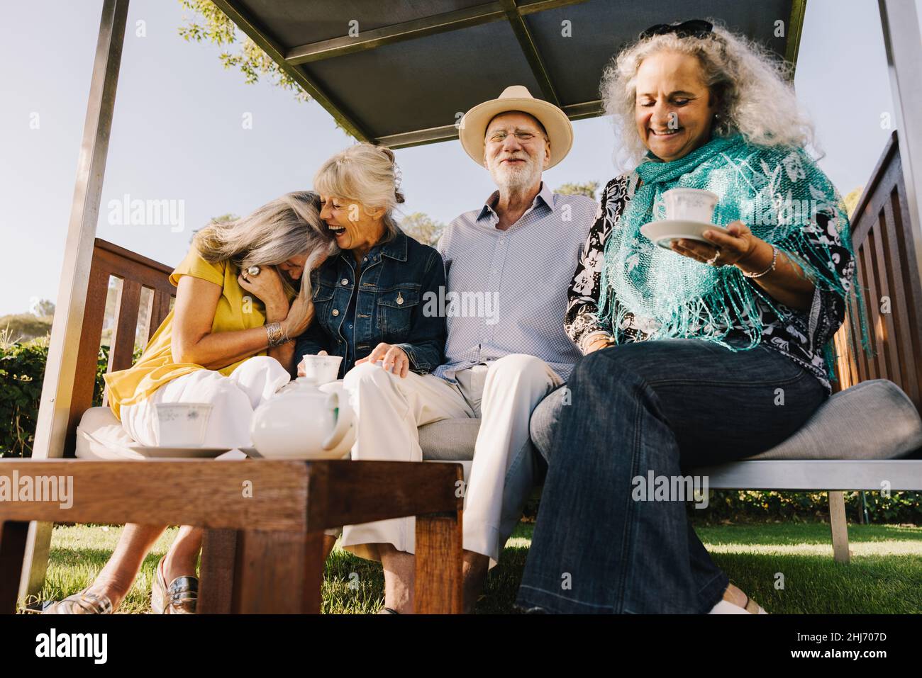 Group of senior friends laughing happily while having tea together. Cheerful elderly friends enjoying their summer vacation at a spa resort. Senior ci Stock Photo