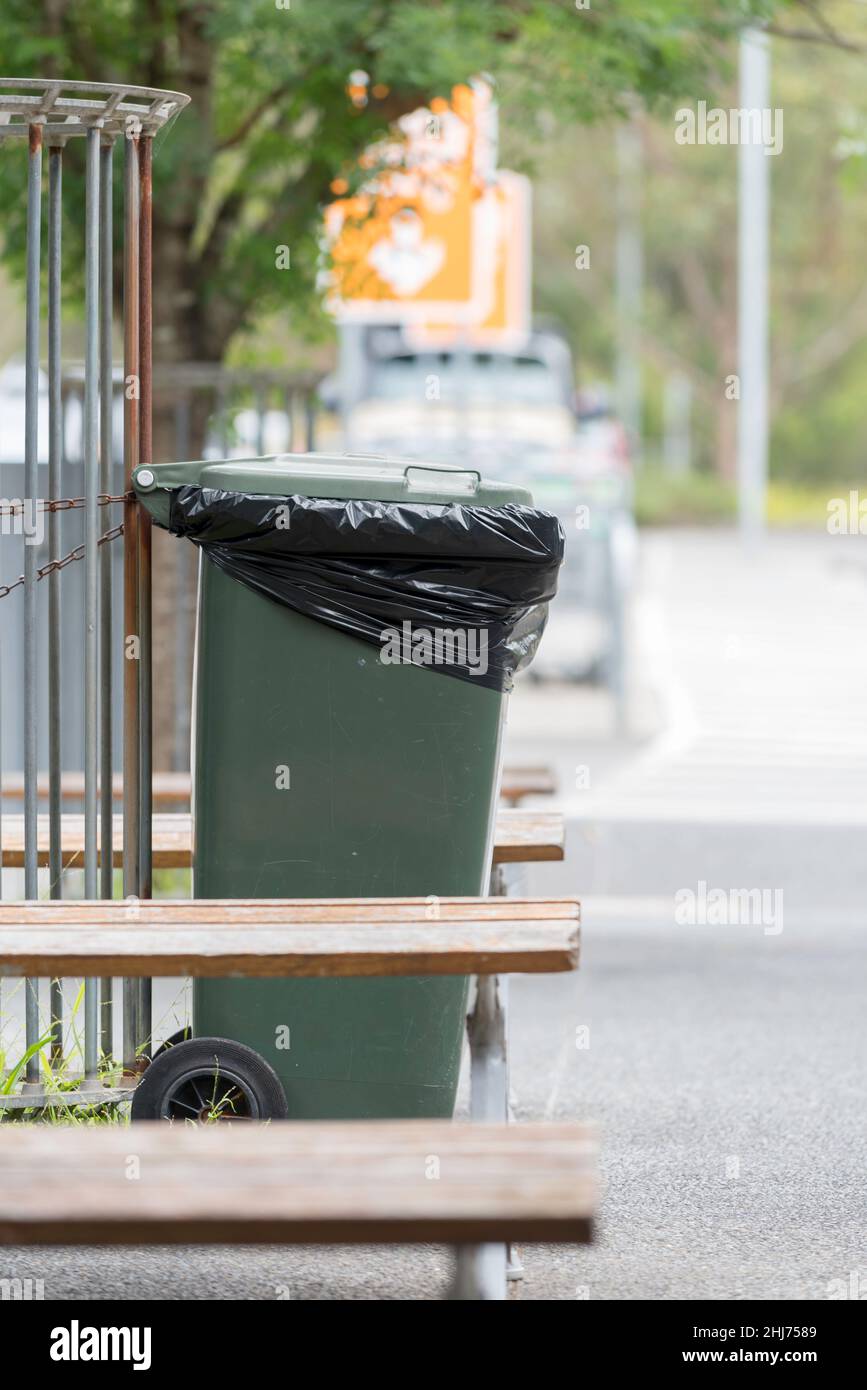 A green sulo or wheely bin with a plastic bag liner, chained to a fence in a shopping centre outside common area in New South Wales, Australia Stock Photo