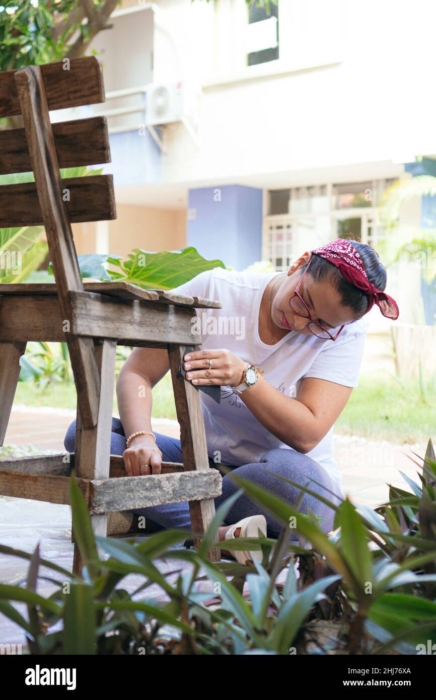 A woman restores and improves an old wooden chair in her home Stock Photo