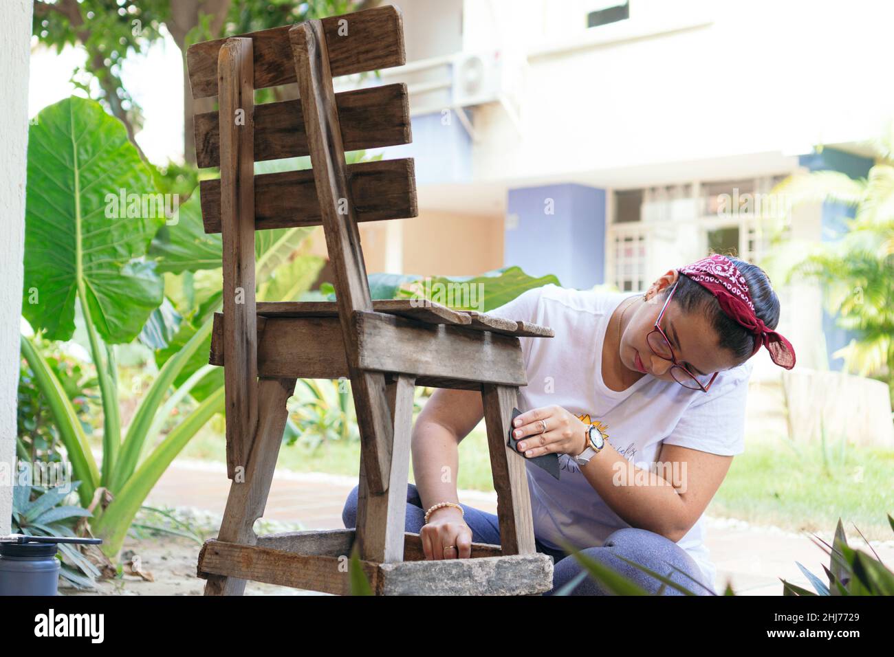Young woman restores and improves an old wooden chair in her home Stock Photo
