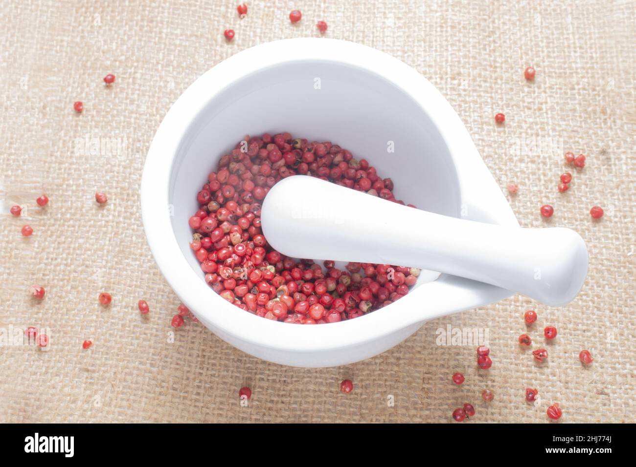 white porcelain mortar and pestle with some loose red peppercorn Stock Photo