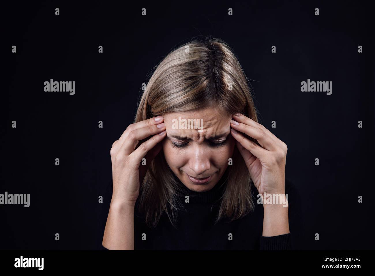 Portrait of crying woman with face down hand fingers touching temples on black background. Victim of physical and psychological abuse. Gaslighting Stock Photo