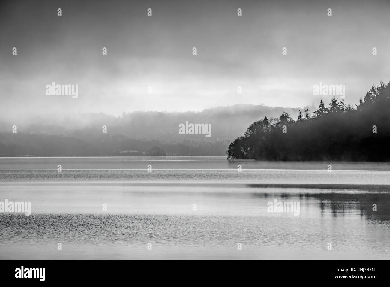Still water and reflections in the early morning on  Windermere from Wray Castle Stock Photo