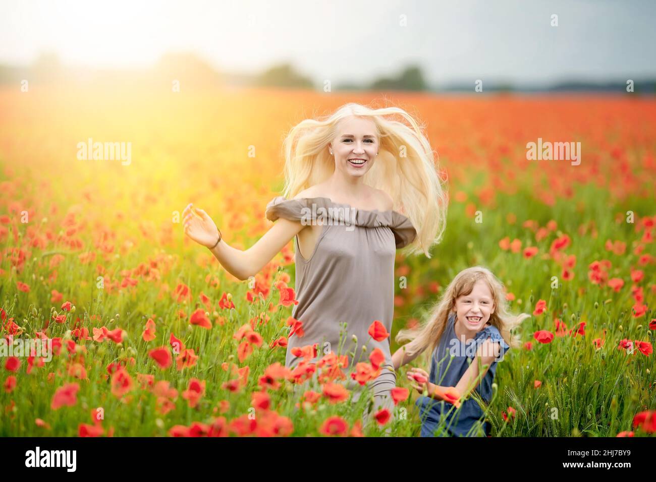 Happy family resting on a beautiful poppy field at sunset. Mom and daughter run around the meadow holding hands. family having fun. Stock Photo