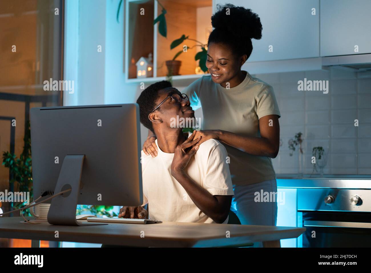 Woman hugging husband from behind while he working on computer remotely from home late at night Stock Photo