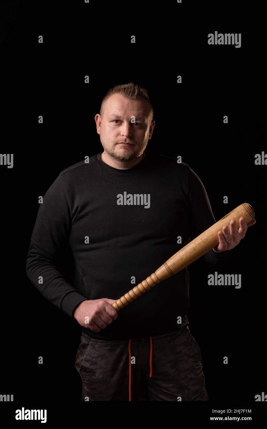 A young man is holding a wooden bat. Bouncer, security guard, bodyguard concept. A large man in a T-shirt looks at the camera. Stock Photo