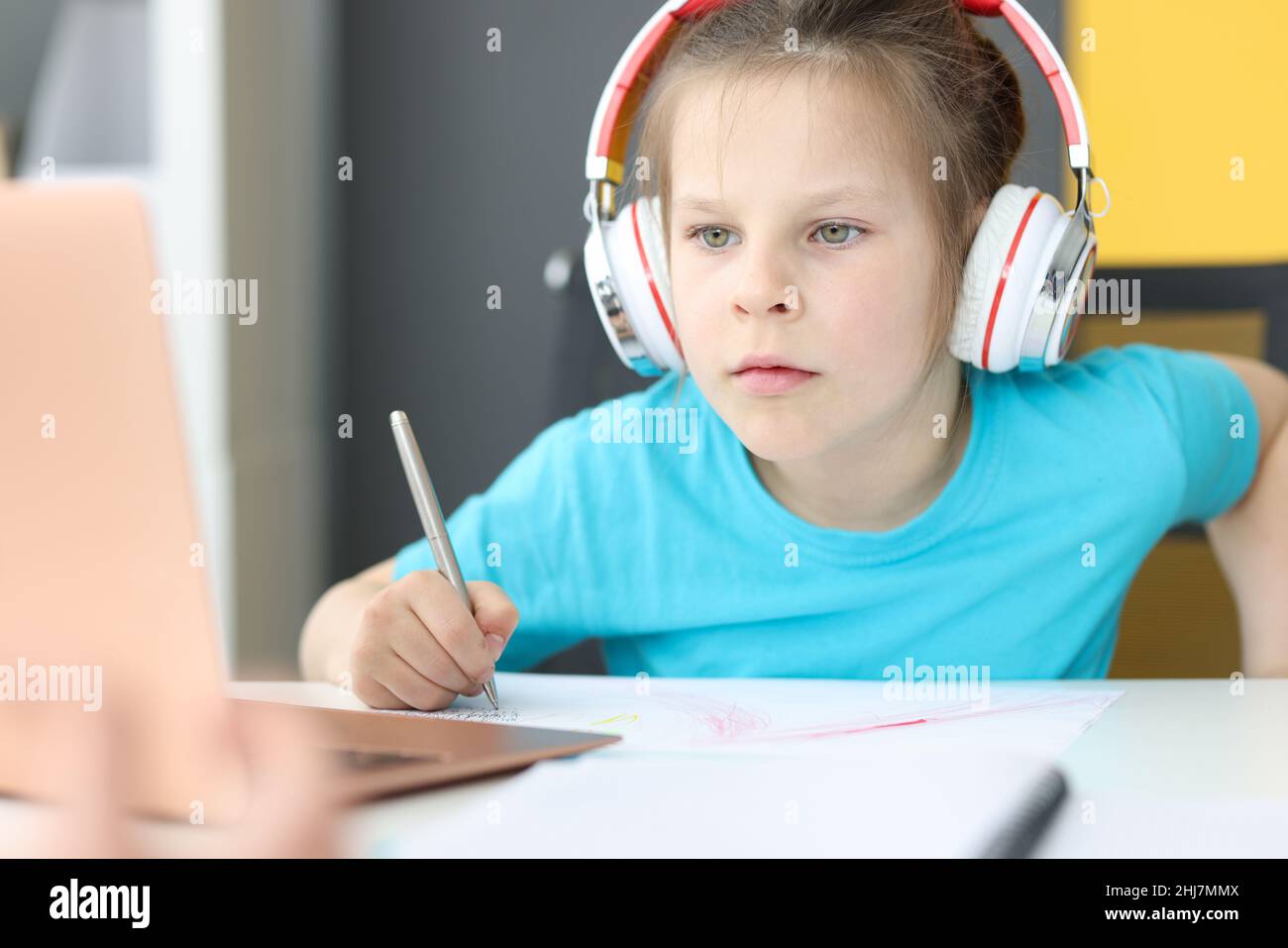 Little girl schoolgirl in headphones sitting in front of laptop at home ...