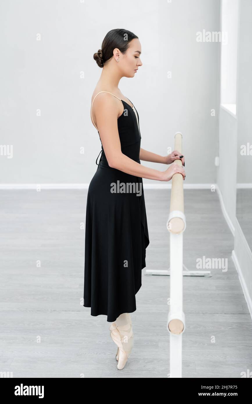 side view of ballet dancer in pointe shoes standing on toe at barre in