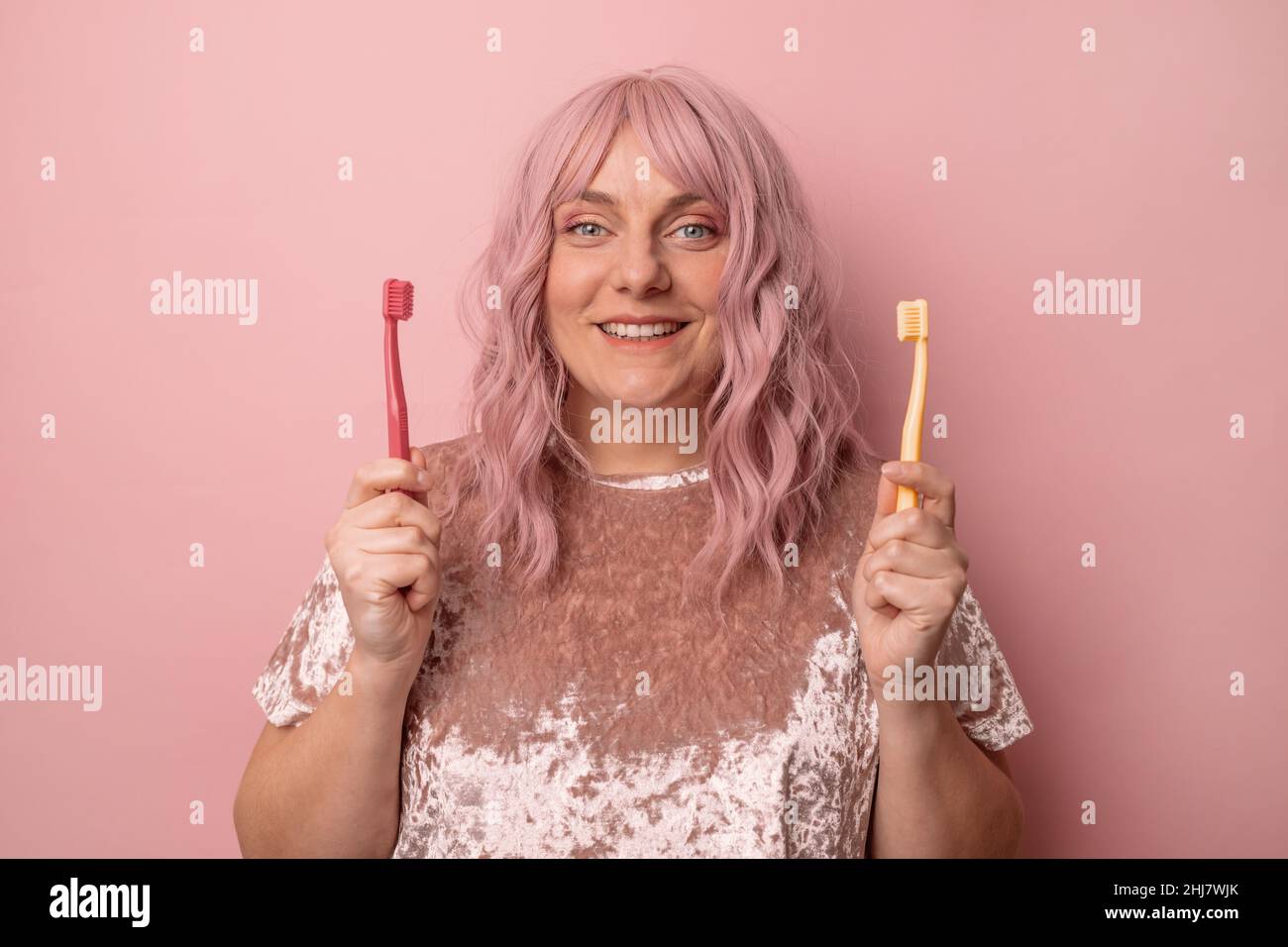 Smiling cheerful funny beautiful attractive young woman with new red and yellow toothbrush on pink background. Banner. Empty place for text Stock Photo