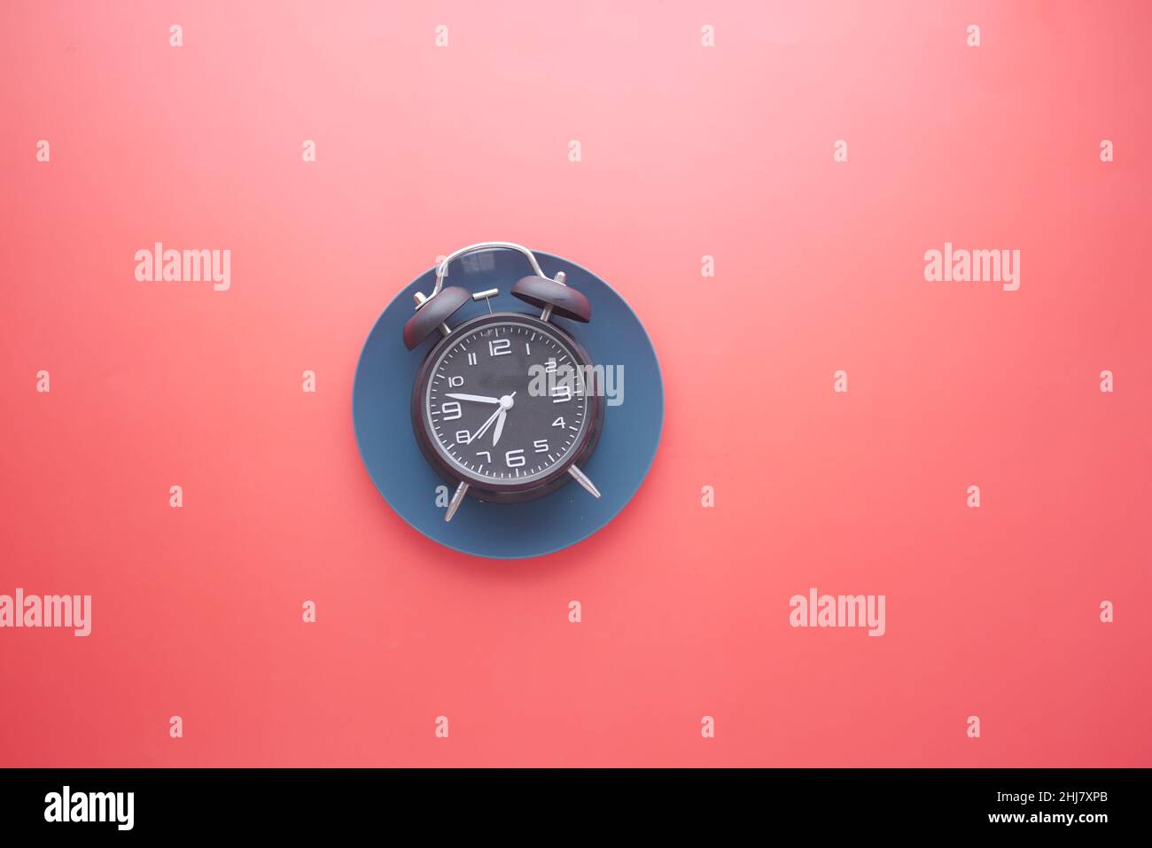 Alarm clock on plate on red background top down  Stock Photo