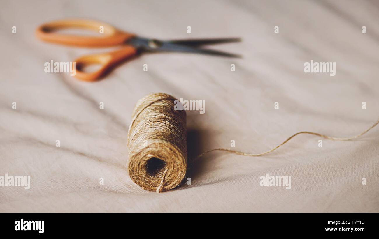 On the beige fabric there are scissors for cutting and a coil of hemp rope. Accessories for the tailor's work. Handmade work. Household items. Stock Photo