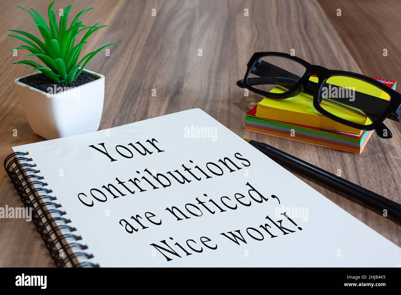 Motivational text on white notepad with potted plan, glasses, a pen and notes on wooden desk. Praise at work concept Stock Photo