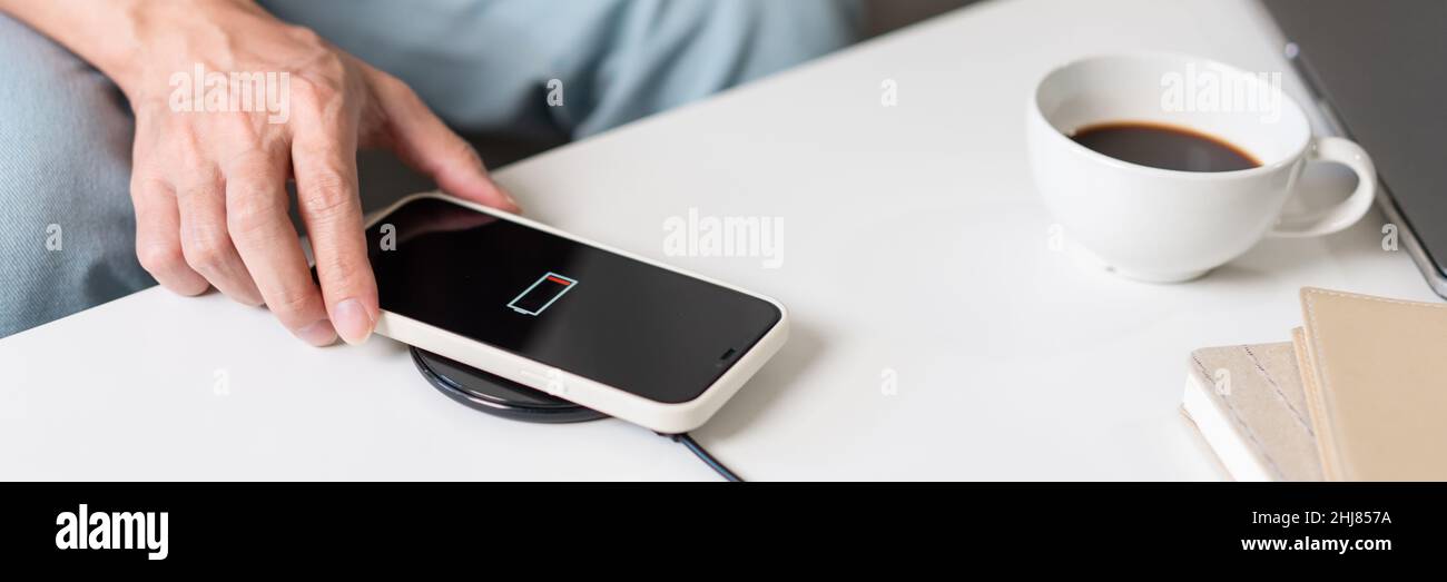 Technology Concept A person with his light blue jeans sitting on the couch and trying to charge his smartphone on the wireless battery charger. Stock Photo