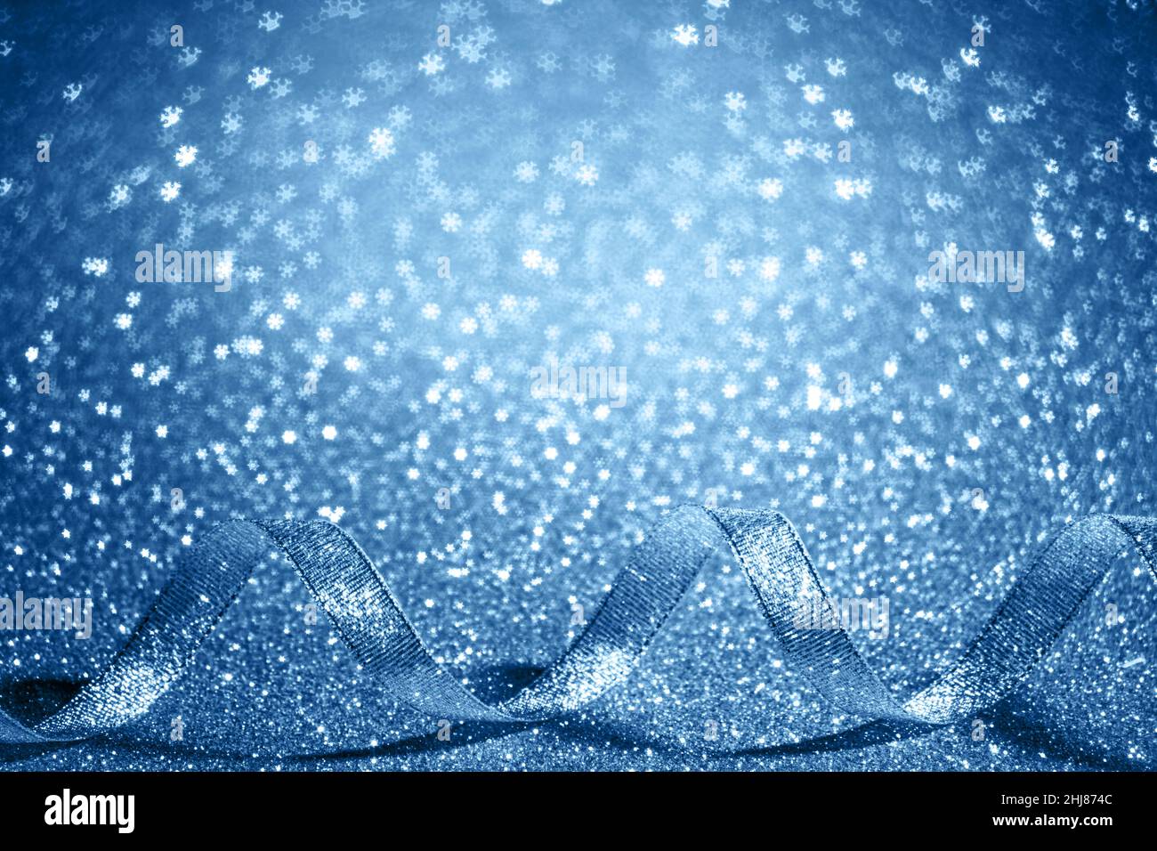 Christmas blue background with free place for text. Shiny serpentine ribbon on an abstract background with shining bokeh snowflakes. Stock Photo