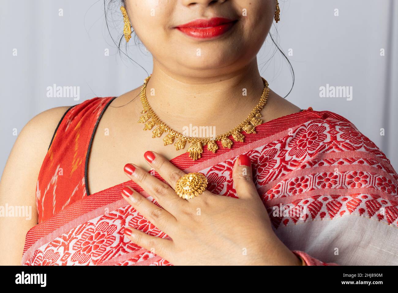 Close up of an Indian woman in red saree wearing gold ornaments with smiling face on white background Stock Photo