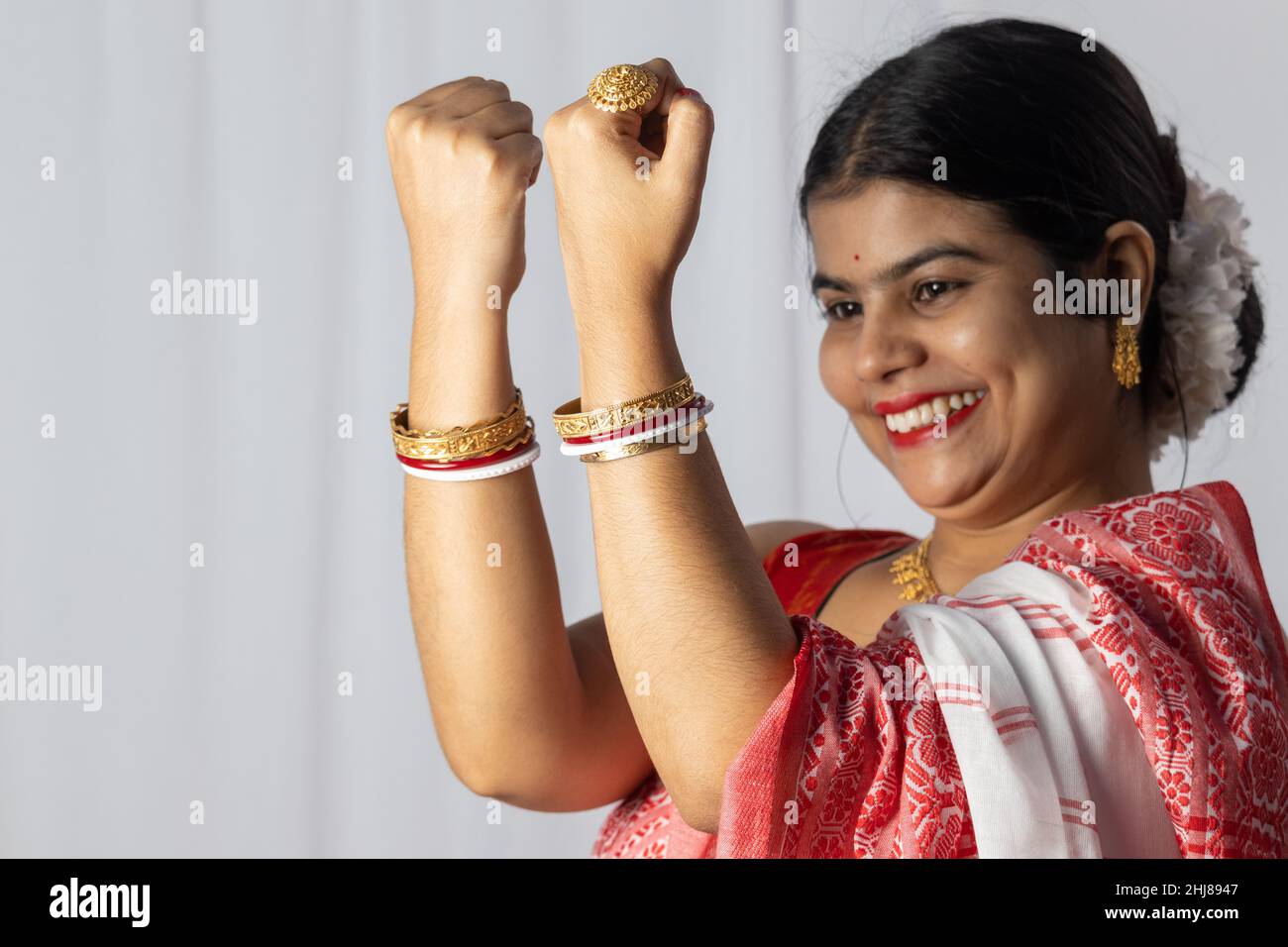 Selective focus on hands of an Indian woman in red saree wearing bangles with smiling face on white background Stock Photo