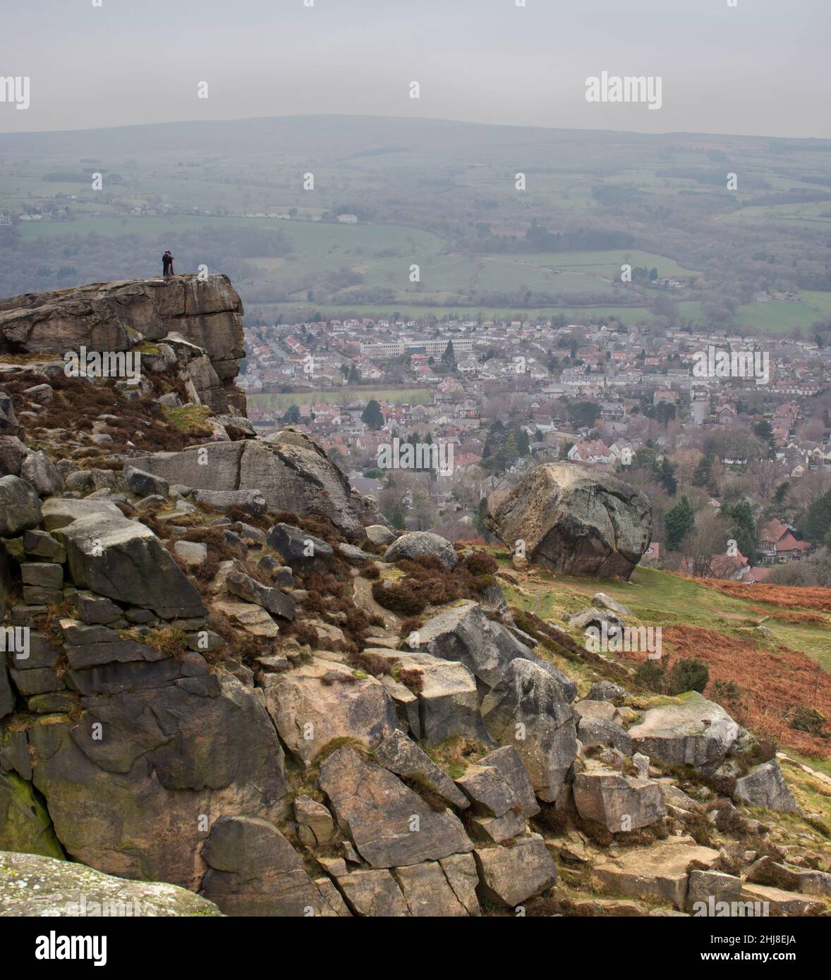 People standing on the edge of the Cow and Calf rock formation, pointing towards the town of Ilkley, below Stock Photo