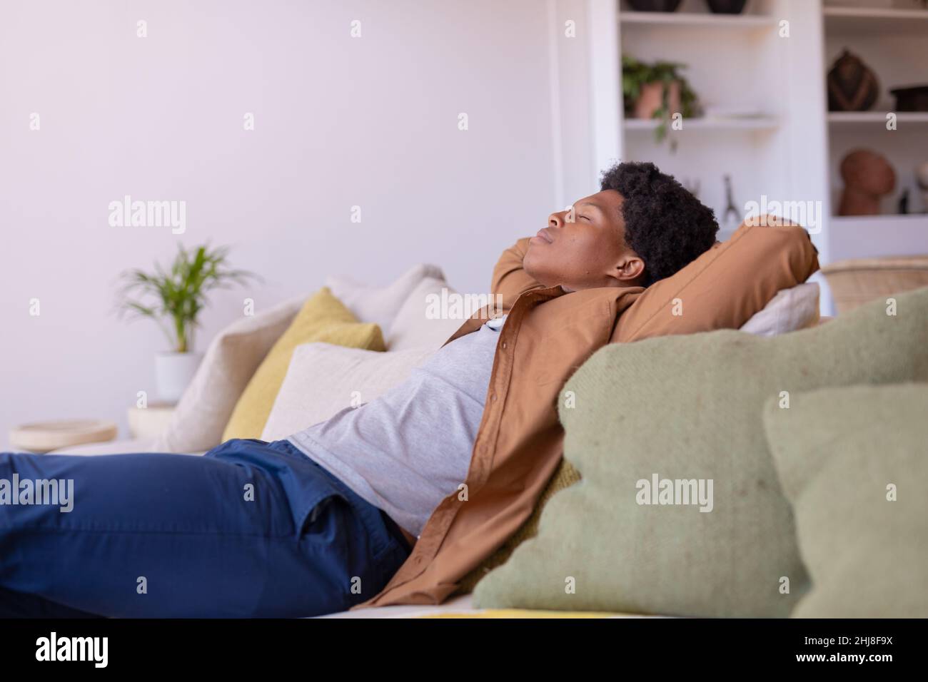 African american young man with eyes closed and hands behind head relaxing on sofa at home. unaltered, sleeping, relaxation, resting, lifestyle, leisu Stock Photo