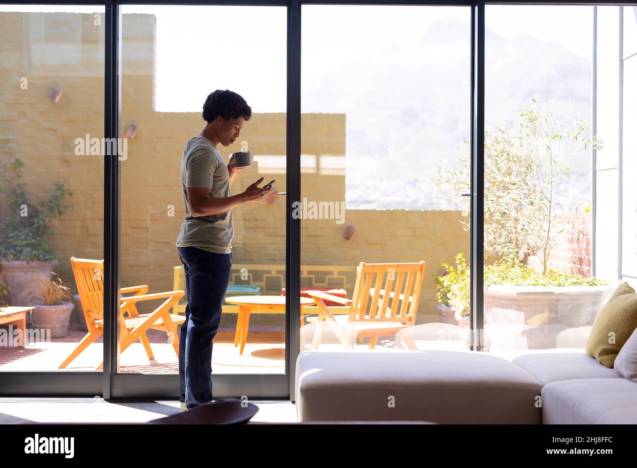 Full length of african american young man using smart phone while standing with coffee cup by window. unaltered, lifestyle, leisure activity, drink, s Stock Photo