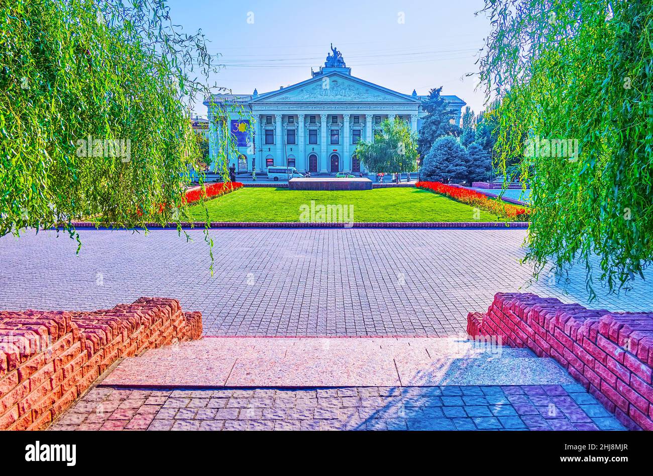 The lush green willow trees and bright flower beds in Theater Square with a view on the Vladimir Magar Dramatic Theater of Zaporizhzhia, Ukraine Stock Photo
