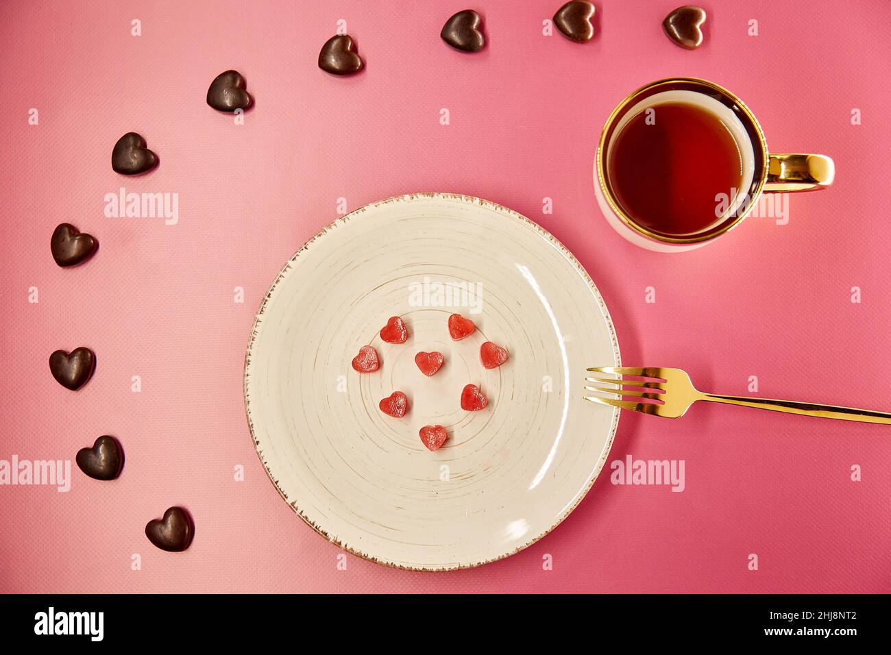 Cute frozen ice hearts on white plate with fork. Chocolate hearts sweets. Creative romantic dinner, Valentines Day concept. Pink gradient background. Top view. Stock Photo