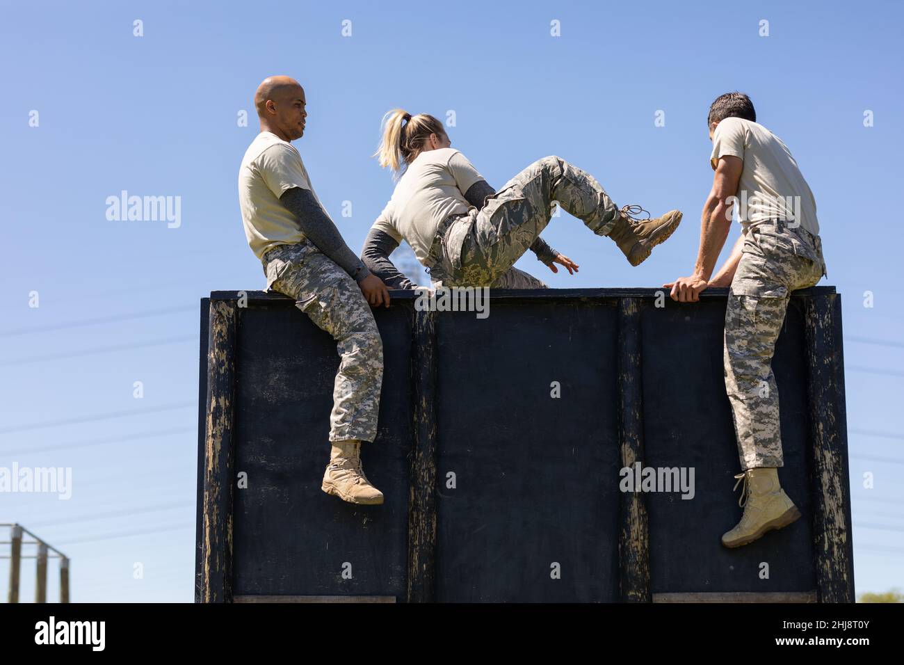 Two diverse male and female soldiers climbing wooden wall during obstacle course at boot camp Stock Photo