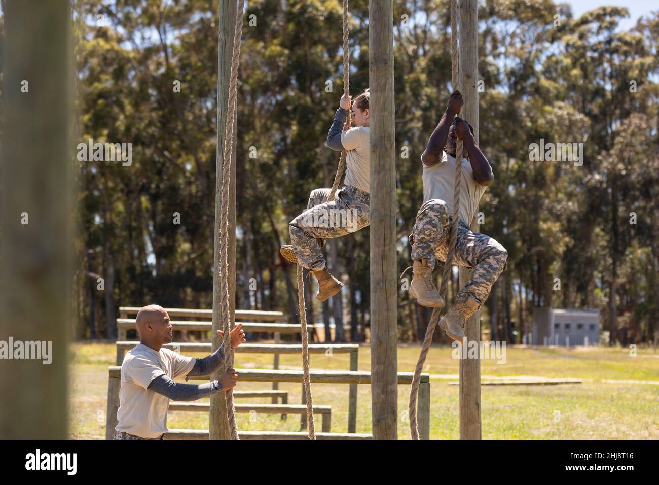 Two diverse male and female soldiers rope climbing during obstacle course at boot camp Stock Photo
