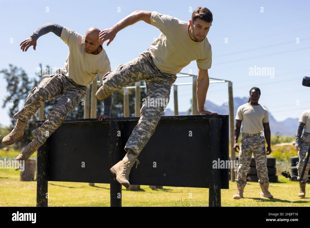 Two diverse male soldiers climbing wooden wall during obstacle course at boot camp Stock Photo
