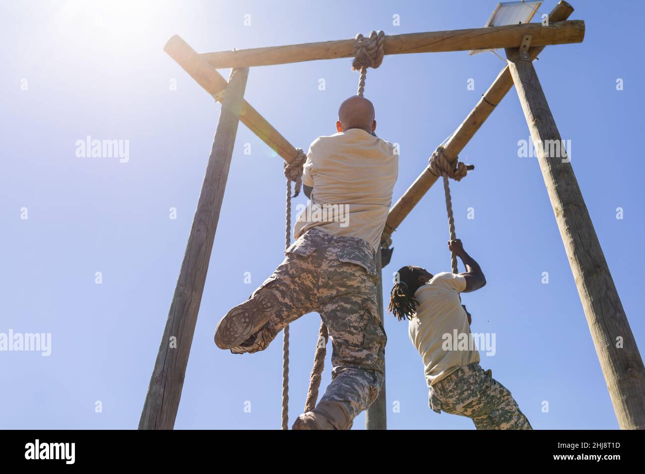 Two african american male soldiers rope climbing during obstacle course at boot camp Stock Photo