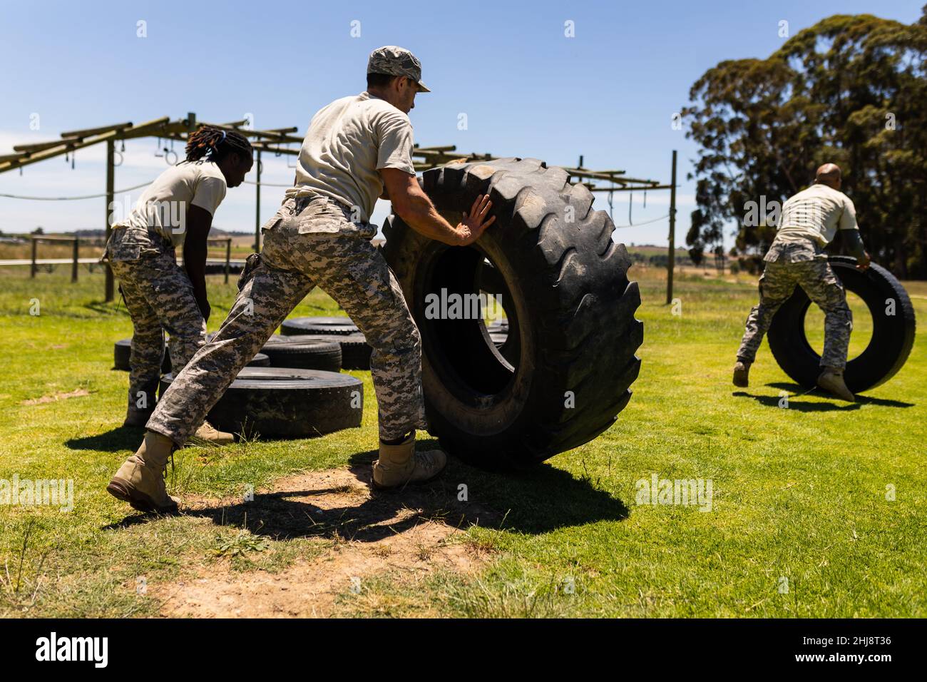 Group of male and female diverse soldiers flipping tires during obstacle course at boot camp Stock Photo
