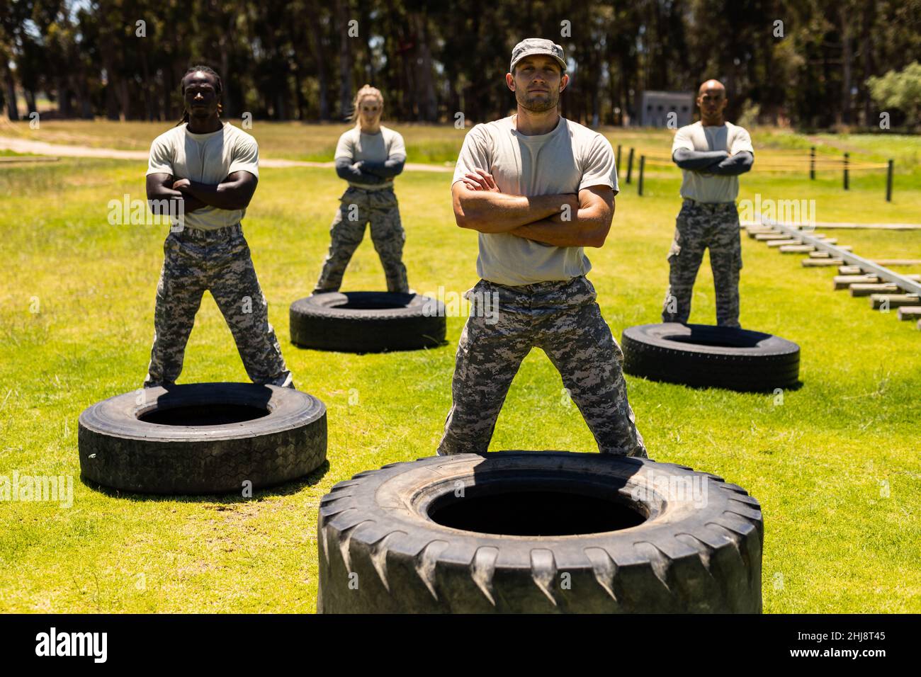 Group of male and female soldiers with arms crossed standing on tire obstacle course at boot camp Stock Photo