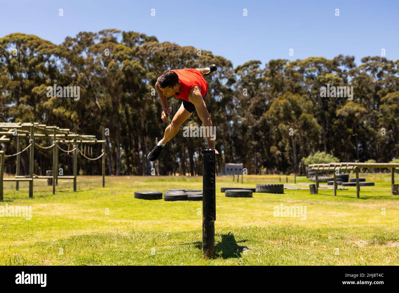 Caucasian fit man jumping over a wooden hurdle during obstacle course at boot camp Stock Photo