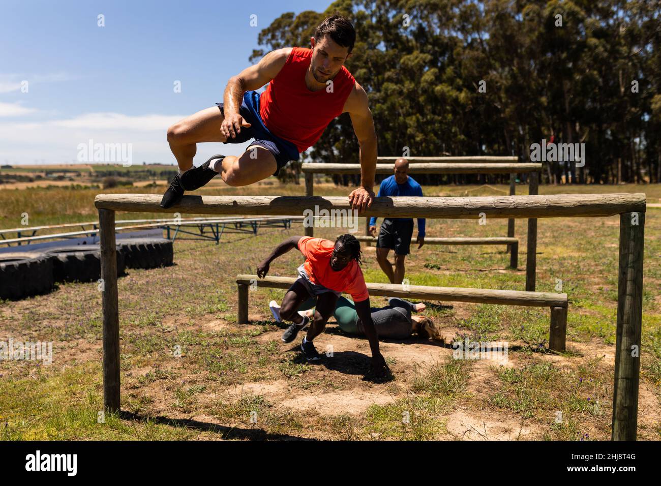 Group of male and female fit people jumping over wooden hurdles during obstacle course at boot camp Stock Photo