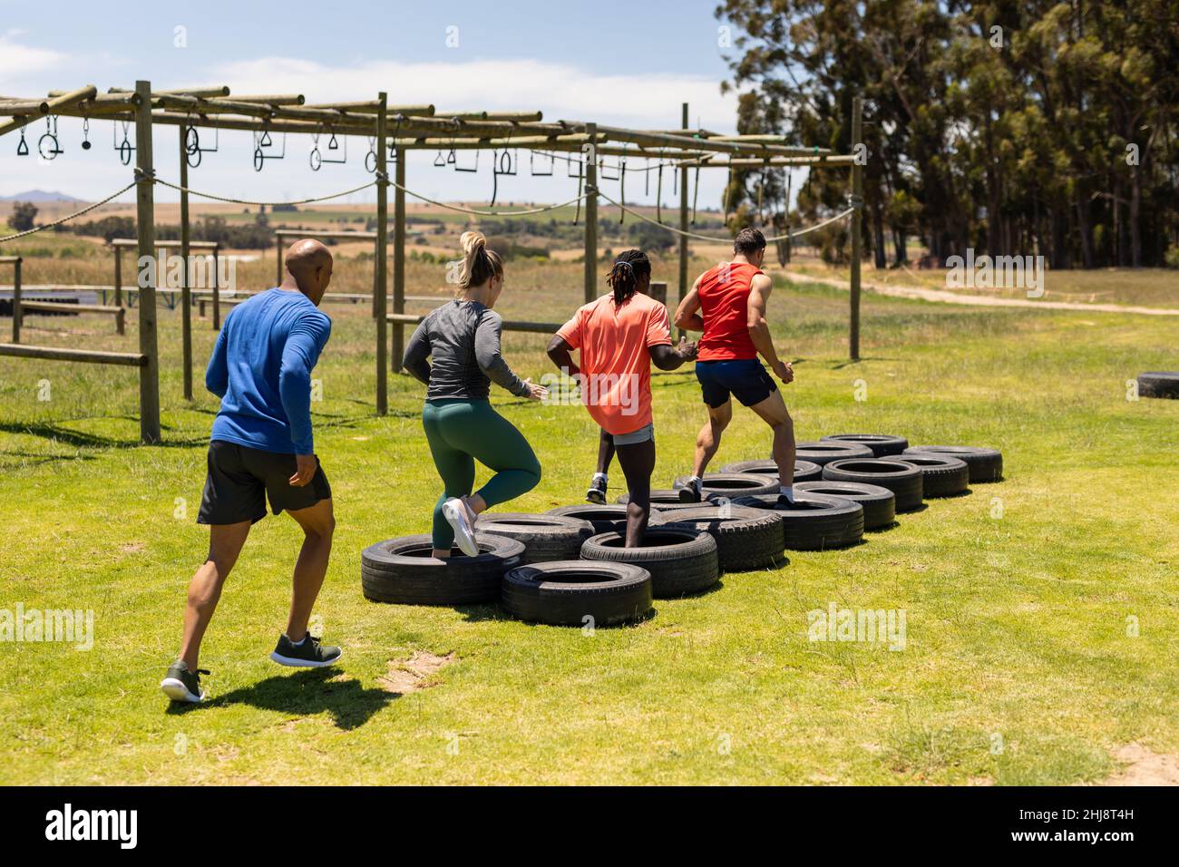 Group of male and female fit people running on tires during obstacle course at boot camp Stock Photo