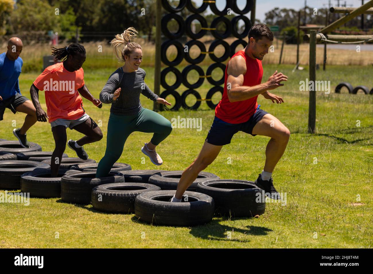 Group of male and female fit people running on tires during obstacle course at boot camp Stock Photo