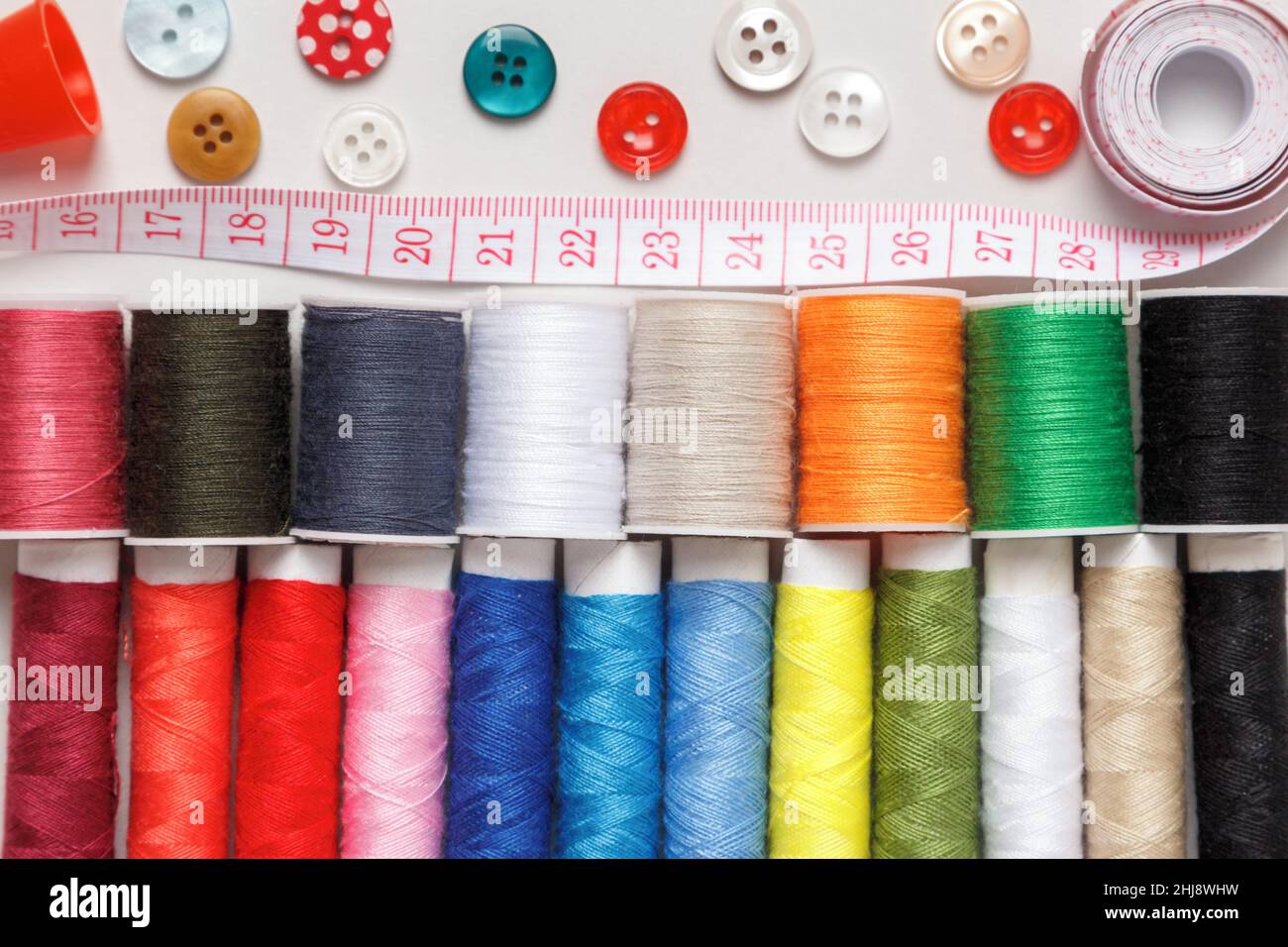 Multi-colored thread buttons measuring tape on a gray background. Stock Photo