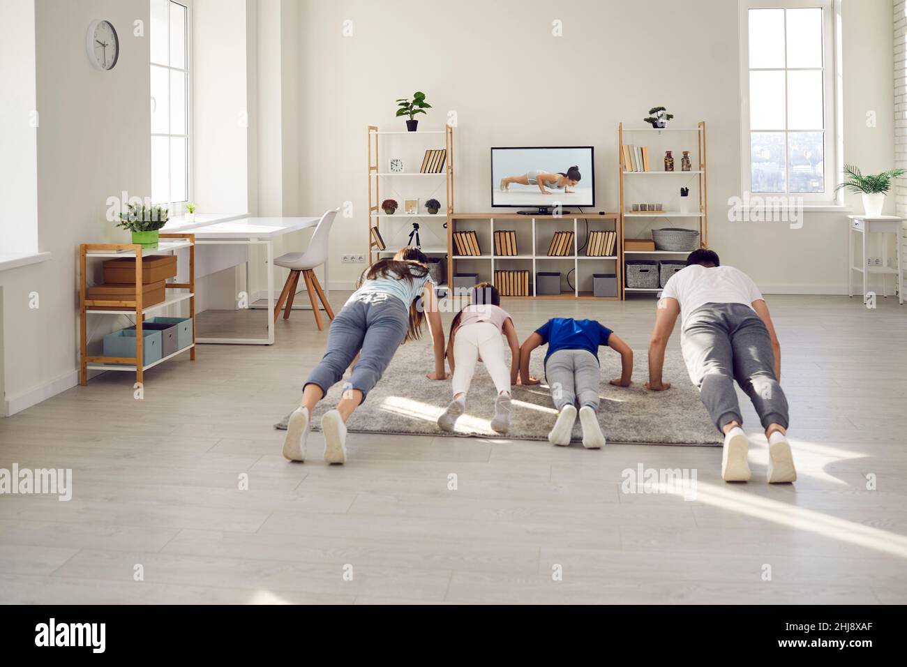 Family watching a fitness workout lesson on TV and doing push ups exercise together Stock Photo