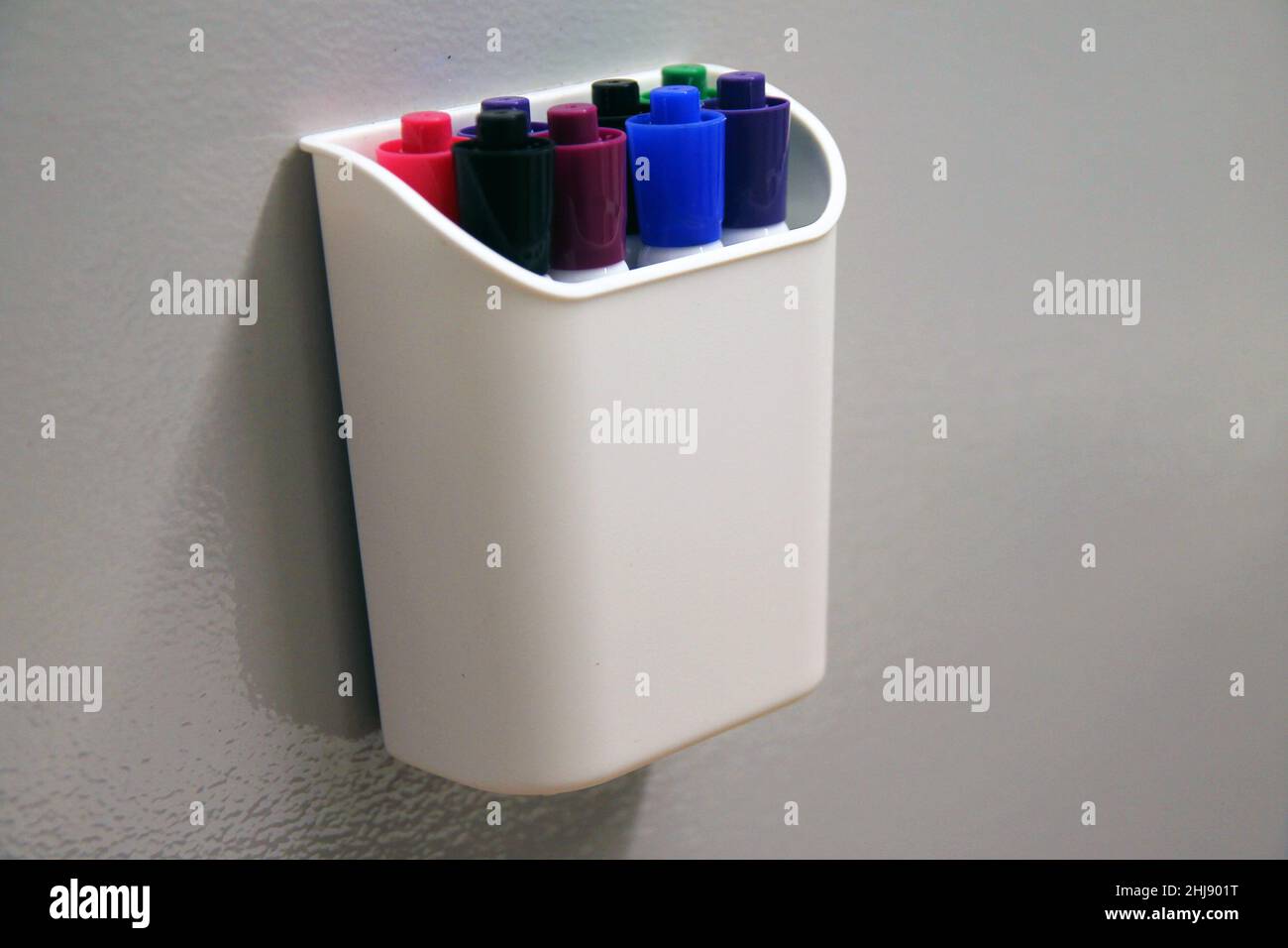 The marking pens in their container hanging on a erasable grey wall of ...