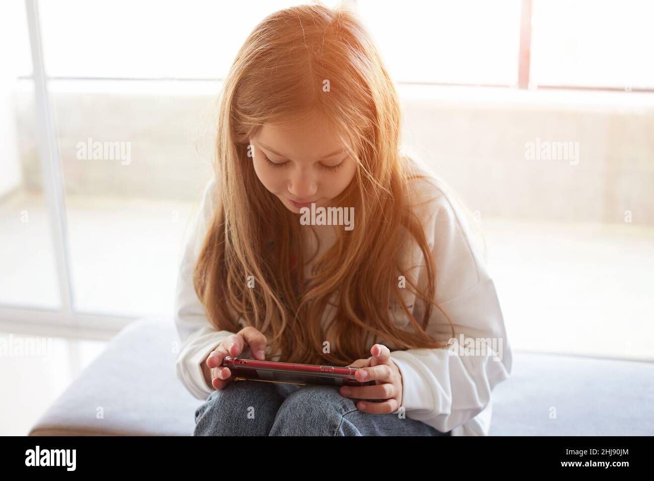 Teen girl checking social media using smartphone at home. Girl relaxing playing mobile games Stock Photo