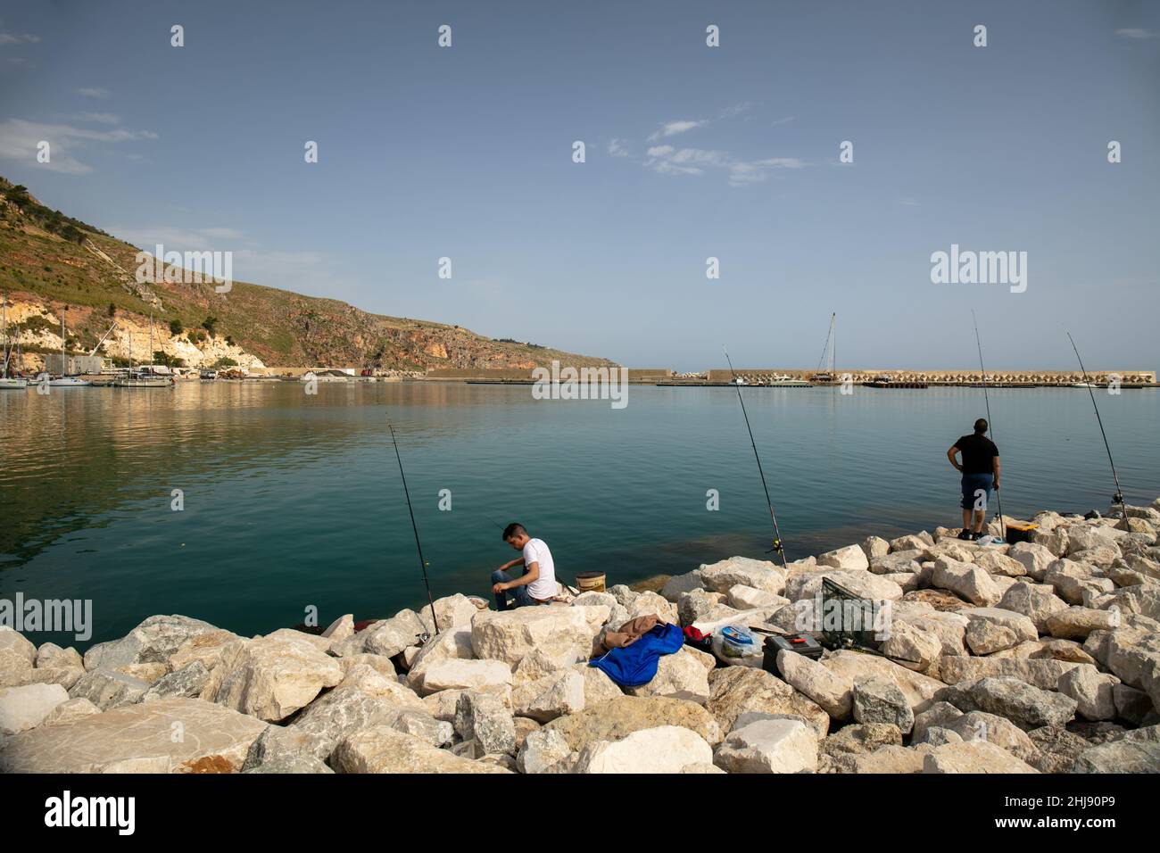 Castellammare del Golfo, Trapani province, Sicily, Italy - May 5 2021: Scenic view of the marina with two fishermen with fishing rods Stock Photo