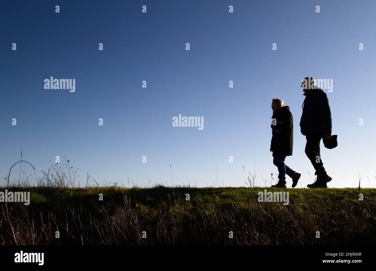 Two People, Elderly Couple Walking On The Sea Wall At Keyhaven, Pennington Marshes Along The Solent Way, Keyhaven UK Stock Photo