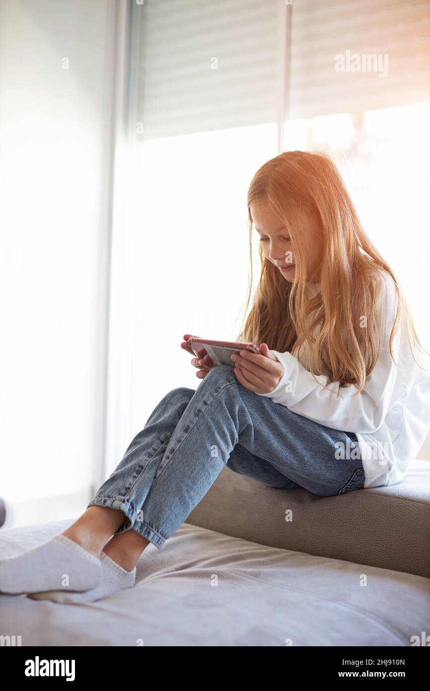 child checking social media using smartphone at home. Girl relaxing playing mobile games Stock Photo