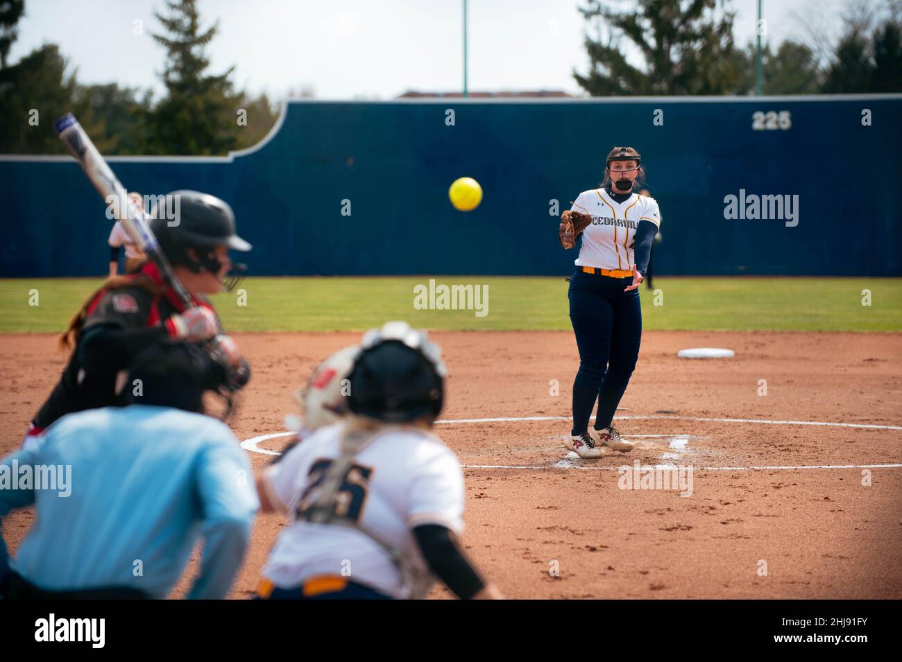 University/college women's softball pitcher pitching the ball in mid air with the batter, catcher, and umpire in the foreground Stock Photo