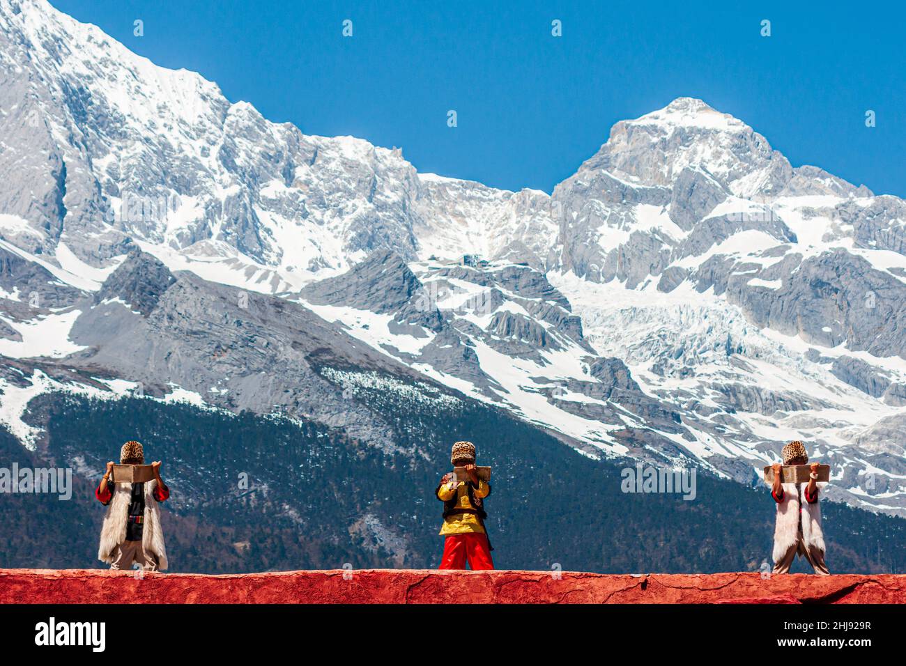 The ethnic minority of the Naxi people in their traditional costumes; scene from a performance with the Jade Dragon Snow Mountain in the background Stock Photo
